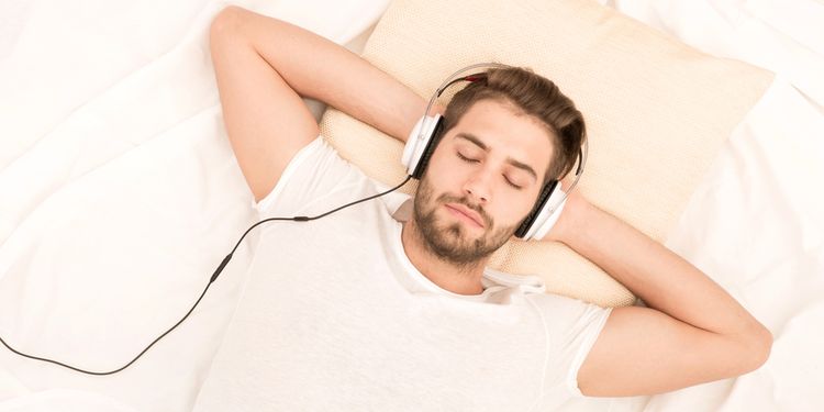 Photo of a man listening binaural beats in bed through head set